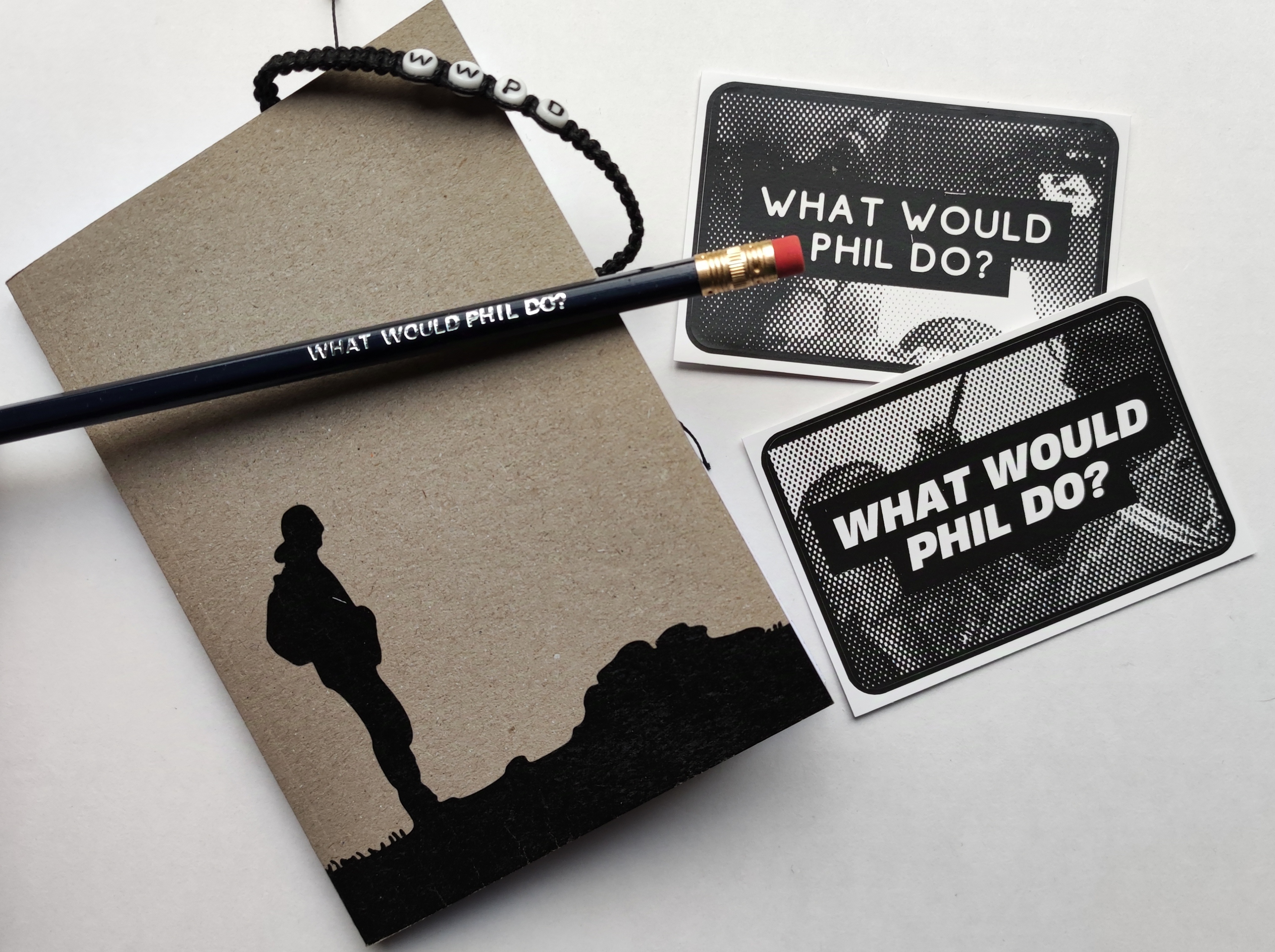 Photo of a notebook, a pencil, a bracelet and two stickers.